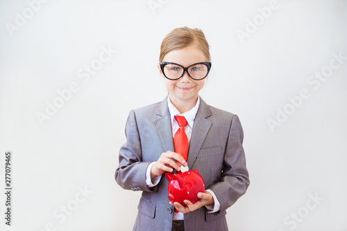 Happy child girl stands in a fashionable suit with a piggy Bank in her hands. Success, creative and innovation business concept © irena_geo