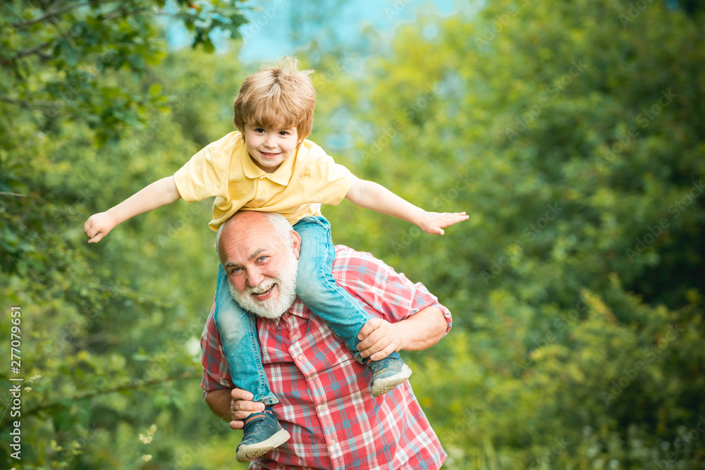 Happy child playing with toy wings arms against summer sky background. Grandfather and Grandson playing - Family Time Together. Happy child playing with toy wings arms against summer sky background. Grandfather and Grandson playing - Family Time Together.