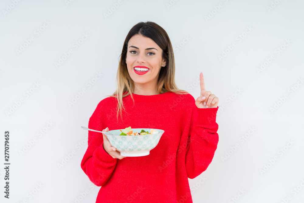 Young woman eating fresh healthy salad over isolated background surprised with an idea or question pointing finger with happy face, number one Young woman eating fresh healthy salad over isolated background surprised with an idea or question pointing finger with happy face, number one