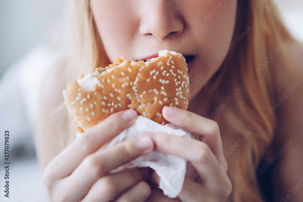 Young girl lies in her bed and eating hamburger in the morning Young girl lies in her bed and eating hamburger in the morning