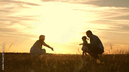 Mom and Dad playing with their daughter in park at sunset. kid takes the first steps. Happy family playing with the child in rays of sun. baby goes from dad to mom and laughs. Slow motion.