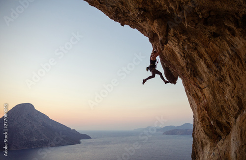 Young woman climbing challenging route at sunset
