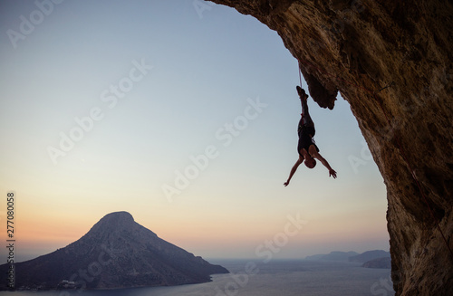 Young female rock climber hanging on rope upside down while being lowered down