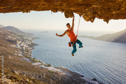 Rock climber hanging on cliff with one hand and showing thumb up