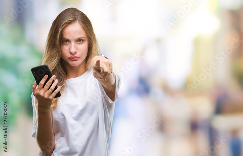 Young beautiful blonde woman using smartphone over isolated background pointing with finger to the camera and to you, hand sign, positive and confident gesture from the front