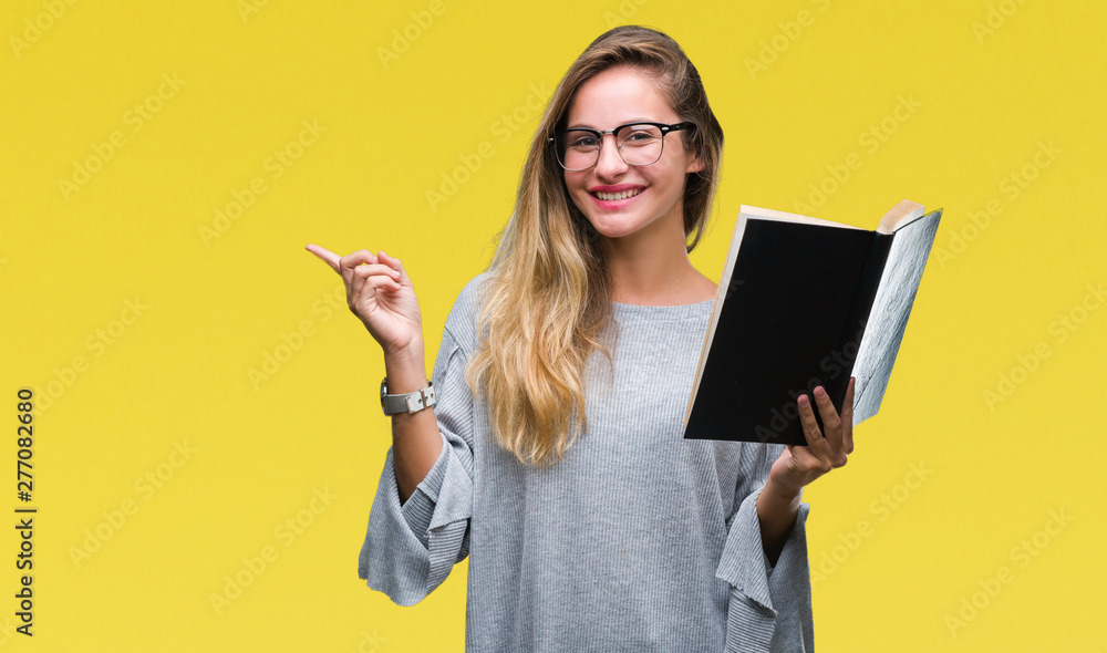 Young beautiful blonde woman reading a book over isolated background very happy pointing with hand and finger to the side Young beautiful blonde woman reading a book over isolated background very happy pointing with hand and finger to the side