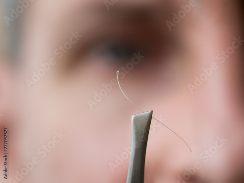 Foto Gray hair on tweezers on the background the face