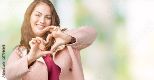 Beautiful plus size young woman wearing winter coat over isolated background smiling in love showing heart symbol and shape with hands. Romantic concept.