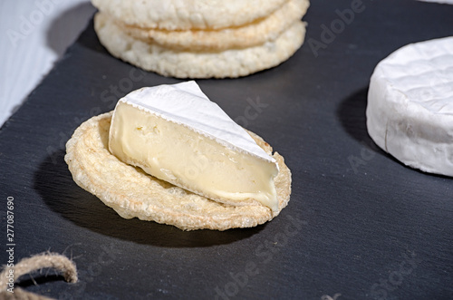 brie de famille cheese and small round loaves lie on a slate Board on a white wooden background, round cheese, sliced cheese on bread.