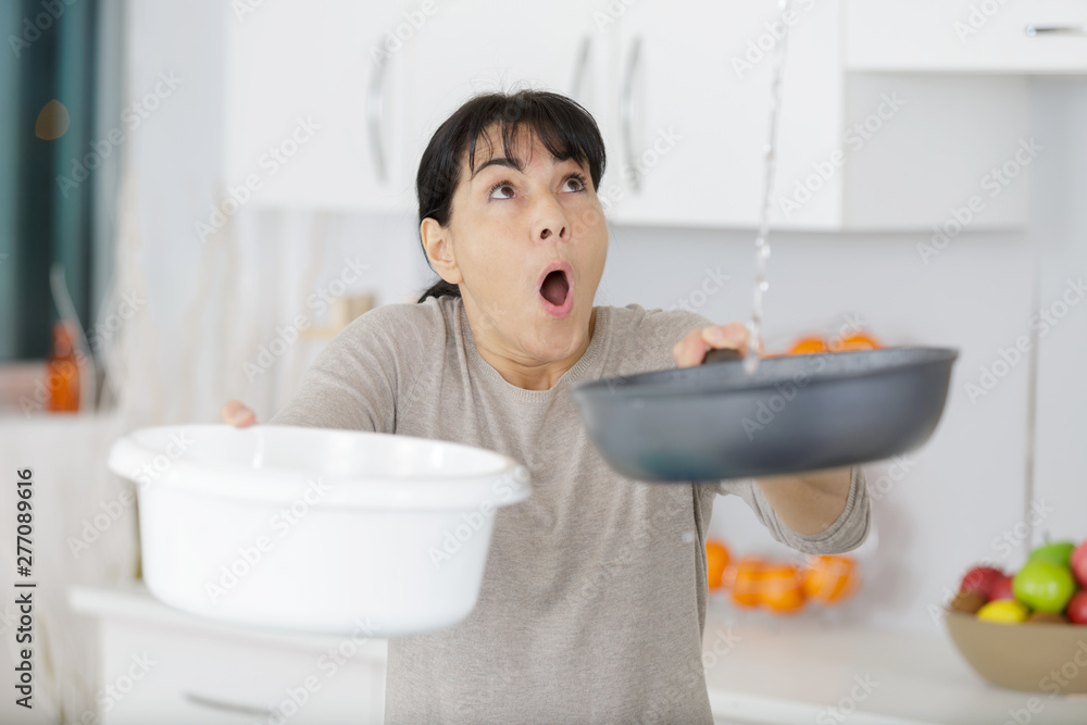 woman holding bucket while water droplets leak from ceiling - obrazy, fototapety, plakaty 