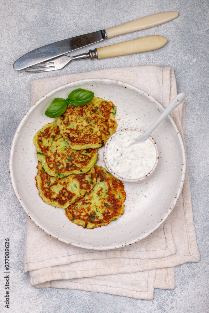 Fritters of zucchini with fresh parsley and Basil. Delicatessen vegetable pancakes with sauce from sour cream and dill. Selective focus Fritters of zucchini with fresh parsley and Basil. Delicatessen vegetable pancakes with sauce from sour cream and dill. Selective focus