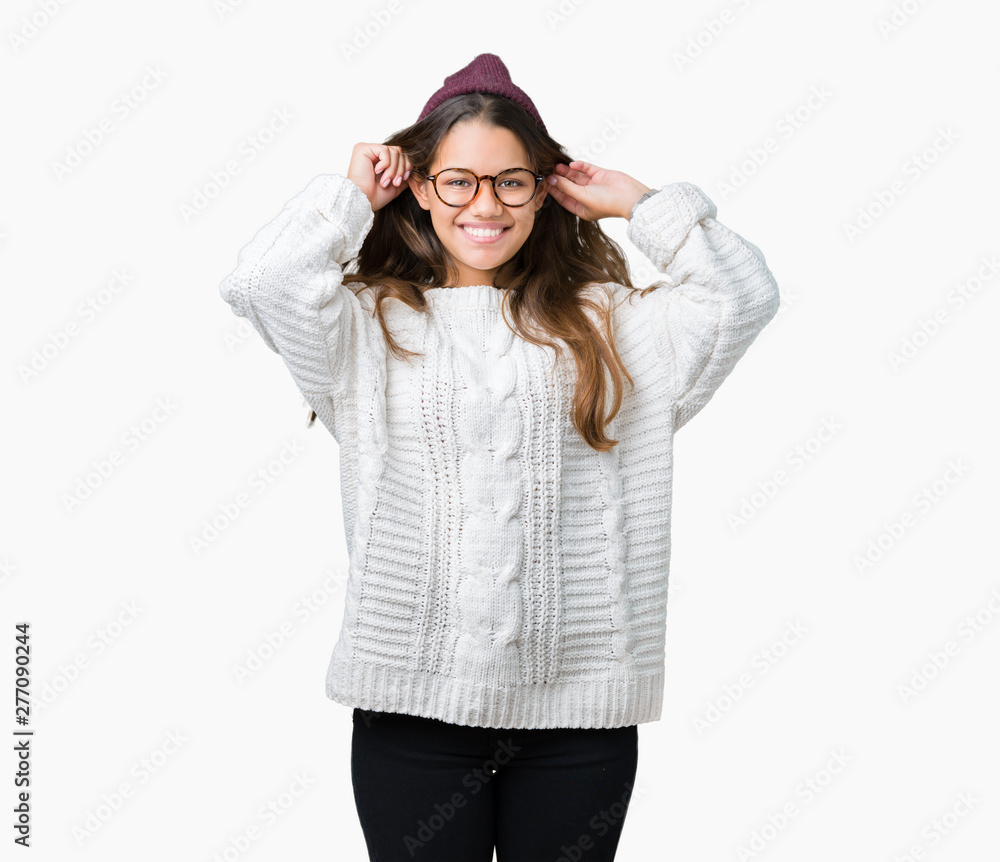 Young beautiful brunette hipster woman wearing glasses and winter hat over isolated background Smiling pulling ears with fingers, funny gesture. Audition problem Young beautiful brunette hipster woman wearing glasses and winter hat over isolated background Smiling pulling ears with fingers, funny gesture. Audition problem