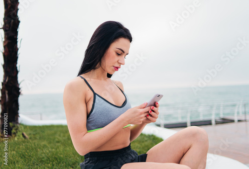 Portrait attractive brunette woman in sportwear holding smartphone on the beach