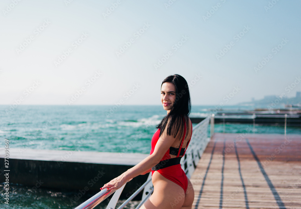 Young fit woman in a red swimsuit sunbathes and posing on the beach