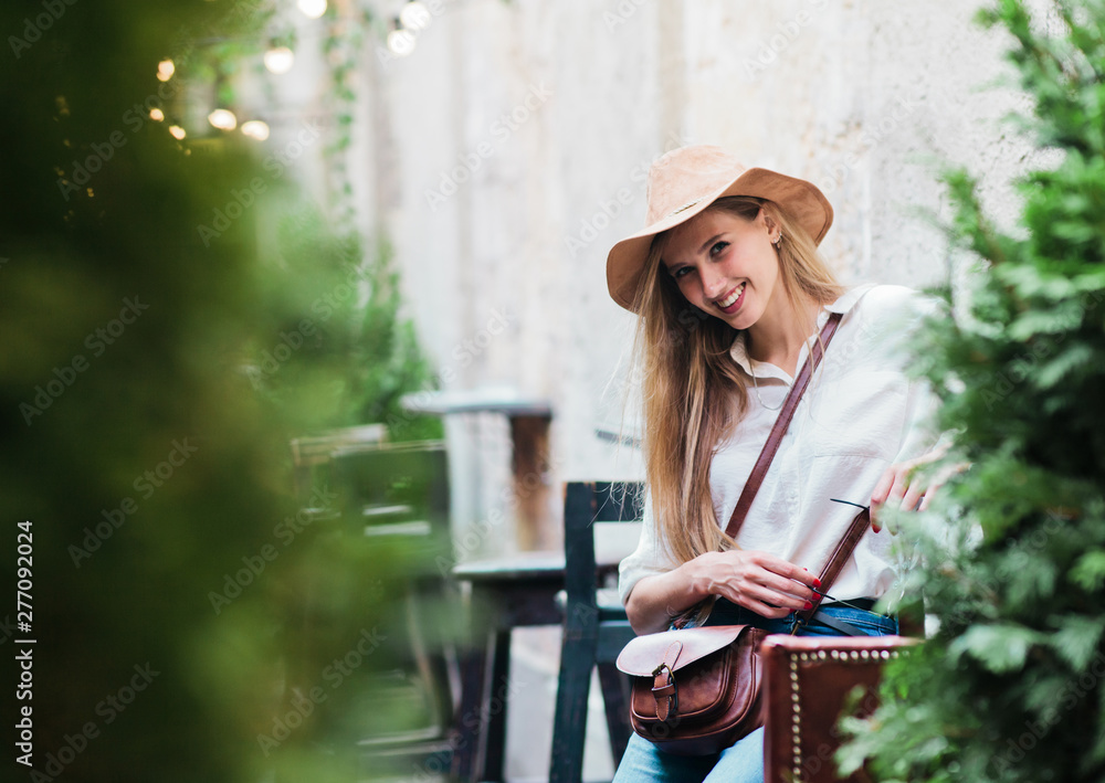 Young blonde woman sitting in vintage style outdoor cafe and looking at camera