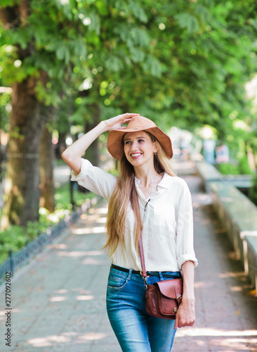 Cheerful blond woman tourist in casual style clothes and felt hat walking through the summer city. Emotional fashion portrait