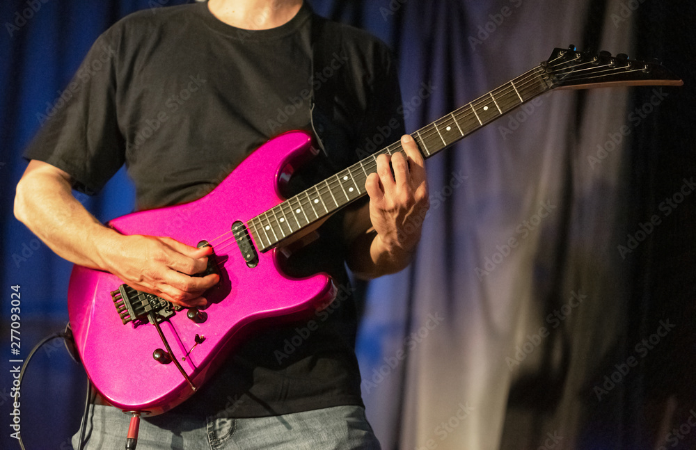 Musician playing pink electric guitar on stage .
