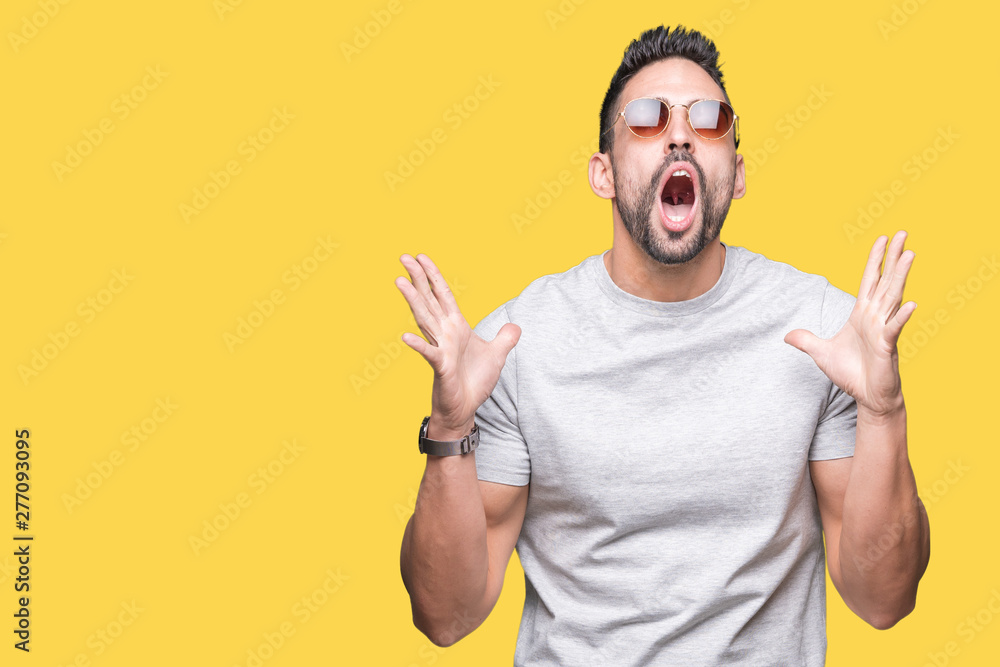 Young handsome man wearing sunglasses over isolated background crazy and mad shouting and yelling with aggressive expression and arms raised. Frustration concept. Young handsome man wearing sunglasses over isolated background crazy and mad shouting and yelling with aggressive expression and arms raised. Frustration concept.
