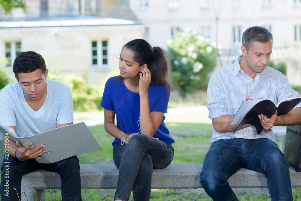 students and teacher sat looking at files on bench outdoors students and teacher sat looking at files on bench outdoors
