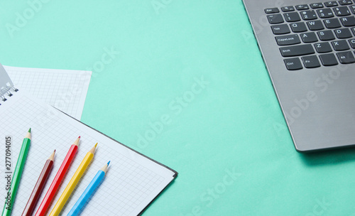 Back to school minimalistic concept. Laptop, color pencils, notebook on blue background.