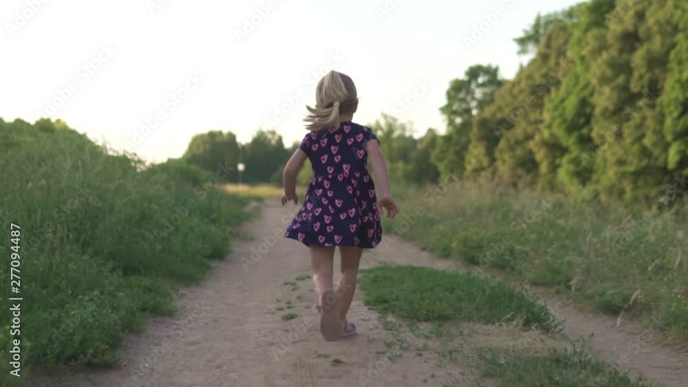 Beautiful little girl running across the field at sunset. Back view. Baby smiles and laughs. Danger, the child runs off to the road with cars Beautiful little girl running across the field at sunset. Back view. Baby smiles and laughs. Danger, the child runs off to the road with cars