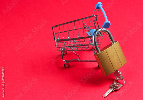 Minimalistic shopping concept. Mini shopping trolley with a lock on red background.