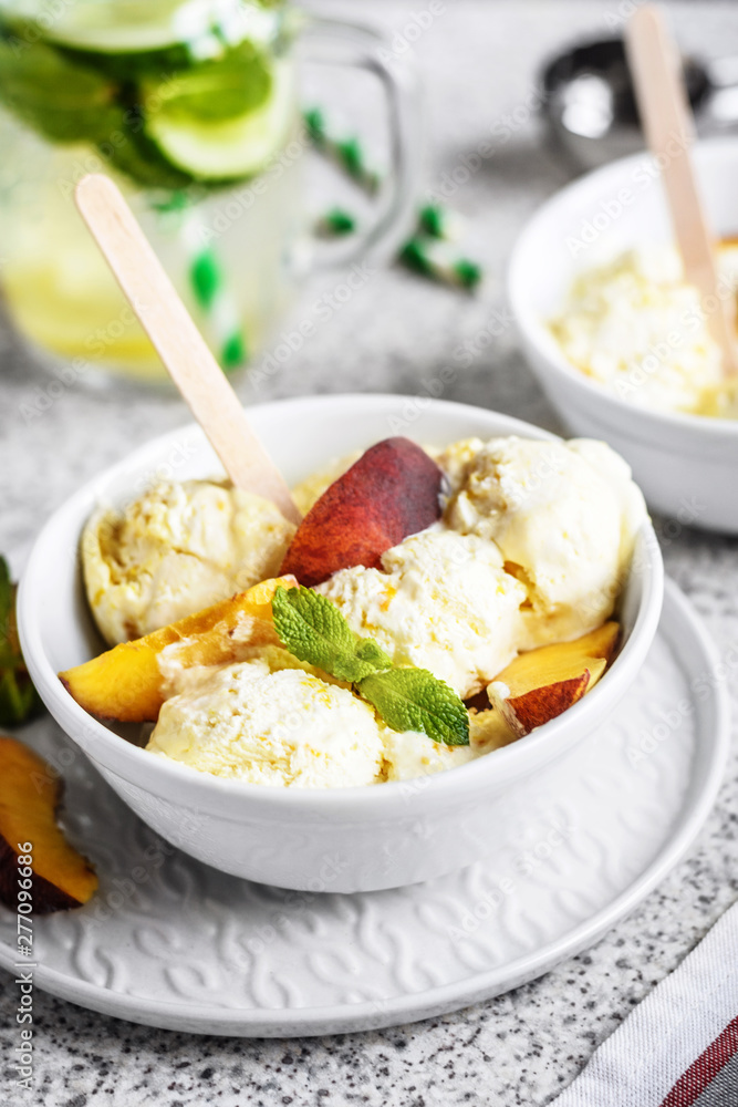  Homemade peach ice cream with mint and fresh peach slices in a plate on a gray background
