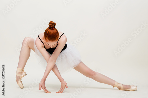 Modern ballet dancer exercising in full body on light grey studio background. Ballerina or modern dancer in black swimsuit dancing on studio background. Redheaded caucasian model on ballet pointe