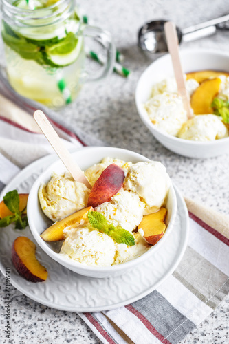  Homemade peach ice cream with mint and fresh peach slices in a plate on a gray background
