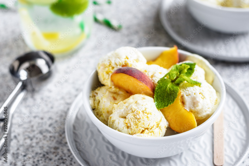 Homemade peach ice cream with mint and fresh peach slices in a plate on a gray background Homemade peach ice cream with mint and fresh peach slices in a plate on a gray background