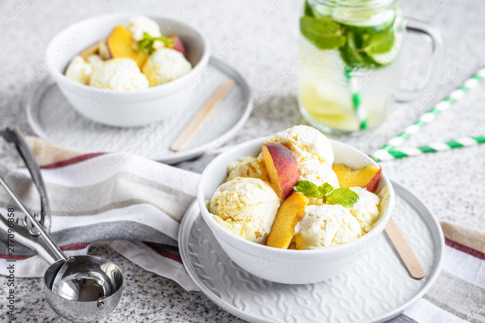 Homemade peach ice cream with mint and fresh peach slices in a plate on a gray background Homemade peach ice cream with mint and fresh peach slices in a plate on a gray background