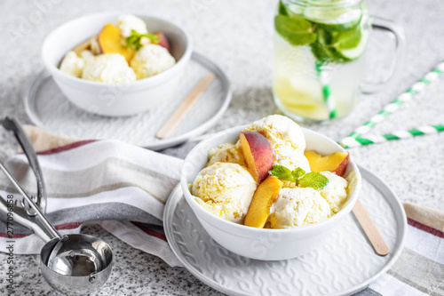  Homemade peach ice cream with mint and fresh peach slices in a plate on a gray background