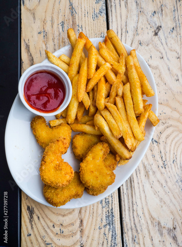 Fried crispy chicken nuggets and french fries with ketchup on white wooden board