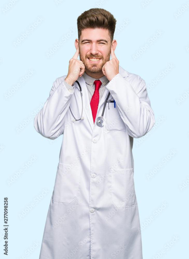 Young handsome doctor man wearing medical coat covering ears with fingers with annoyed expression for the noise of loud music. Deaf concept. Young handsome doctor man wearing medical coat covering ears with fingers with annoyed expression for the noise of loud music. Deaf concept.