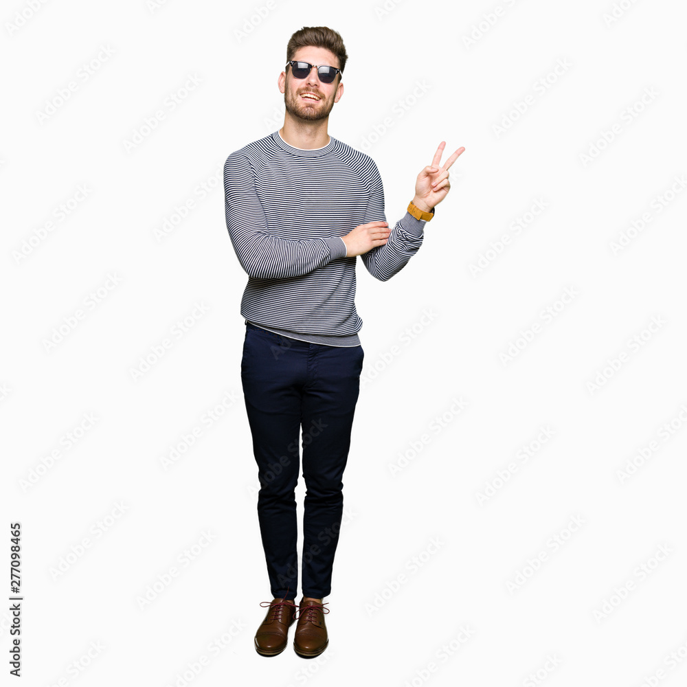 Young handsome man wearing sunglasses smiling with happy face winking at the camera doing victory sign. Number two. Young handsome man wearing sunglasses smiling with happy face winking at the camera doing victory sign. Number two.