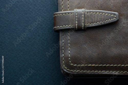 Wallet of rough brown leather, stitched with light-colored threads on a blue background © Kati