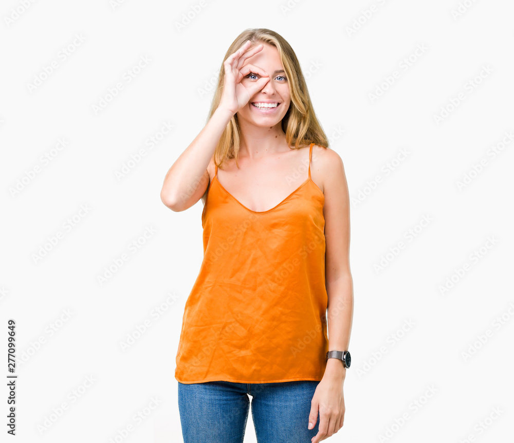 Fototapeta premium Beautiful young woman wearing orange shirt over isolated background doing ok gesture with hand smiling, eye looking through fingers with happy face.