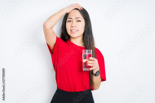 Young brunette woman drinking a glass of water over isolated background stressed with hand on head, shocked with shame and surprise face, angry and frustrated. Fear and upset for mistake.