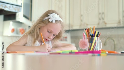 A cute little girl sits at her desk and draws with pencils photo