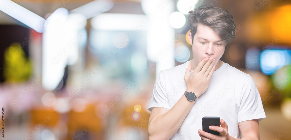 Young man using smartphone over isolated background cover mouth with hand shocked with shame for mistake, expression of fear, scared in silence, secret concept Young man using smartphone over isolated background cover mouth with hand shocked with shame for mistake, expression of fear, scared in silence, secret concept