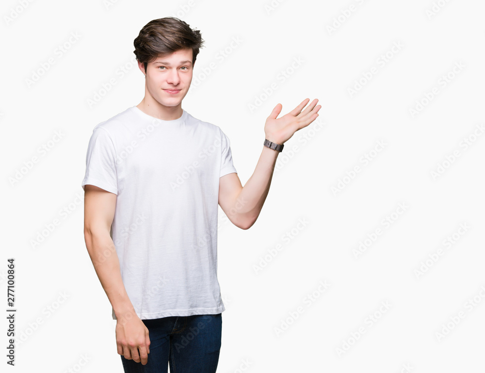 Young handsome man wearing casual white t-shirt over isolated background smiling cheerful presenting and pointing with palm of hand looking at the camera. Young handsome man wearing casual white t-shirt over isolated background smiling cheerful presenting and pointing with palm of hand looking at the camera.