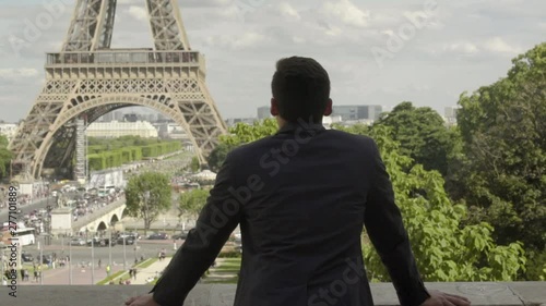 Handsome Businessman posing at the Eiffel Tower after work, with a black jacket, brown hair and tanned skin. Beautiful cloudy blue sky in Paris. 4K. Slow Motion. Peaceful, alone, view, freedom.