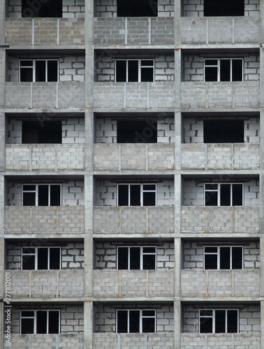 The fragment of the facade of unfinished and abandoned monolithic residential building. Background with windows of the multi-storey building. Verticale frame