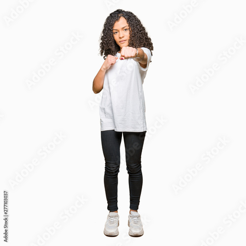 Young beautiful woman with curly hair wearing white t-shirt Punching fist to fight  aggressive and angry attack  threat and violence