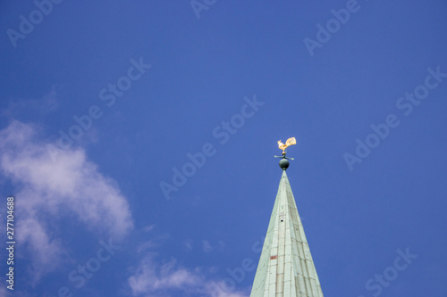 Decorative cock on steeple of ancient tower against blue sky. Weathercock on roof in Bremen, Germany. Spire of medieval church with bird. Wind direction symbol. Travel concept. 