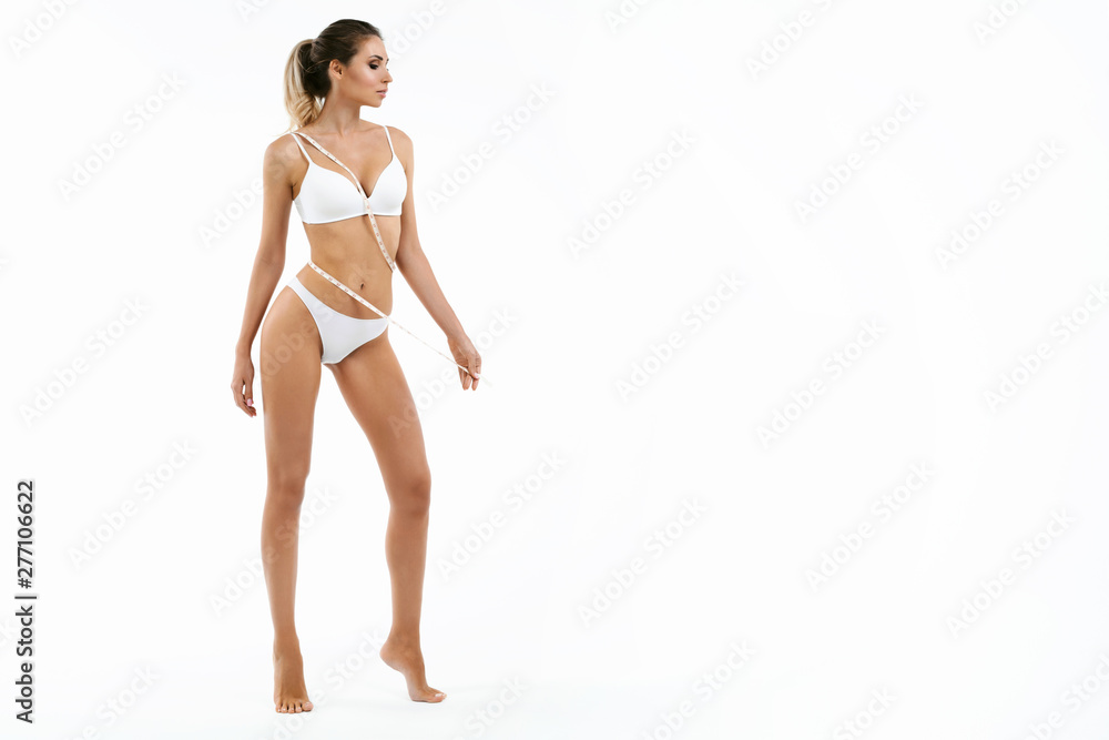 Woman with measure tape. Beauty perfect slim body: fit sporty and healthy woman posing at white background in underwear. Sport, wellness, fitness, diet, weight loss and healthcare concept Woman with measure tape. Beauty perfect slim body: fit sporty and healthy woman posing at white background in underwear. Sport, wellness, fitness, diet, weight loss and healthcare concept