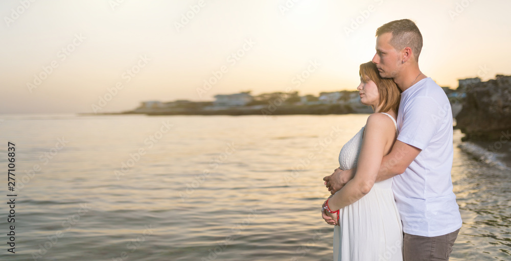 Pregnant woman embracing with her husband on the beach at sunset