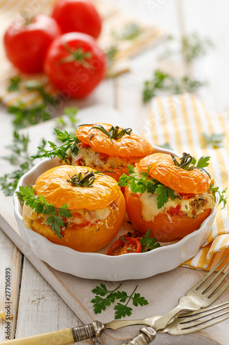 Stuffed tomatoes, baked yellow tomatoes stuffed with bulgur, vegetables and cheese with the addition of aromatic herbs in a baking dish on a white wooden table, close up. Vegetarian food