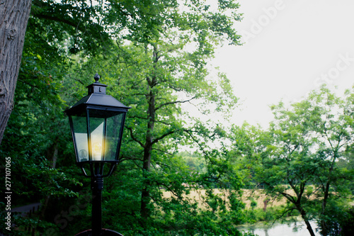 Old lantern on the background of green trees in a park