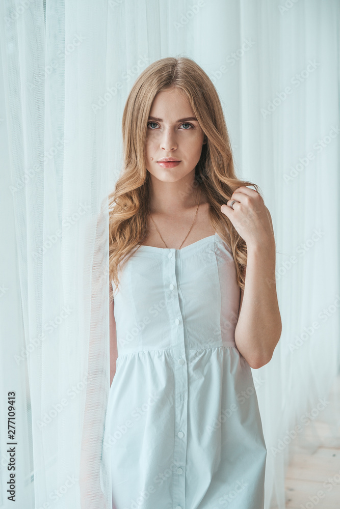 Girl in a light white dress posing by the window. Girl in a light white dress posing by the window.